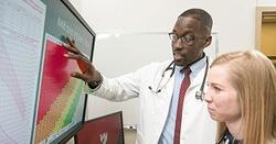 A male and female medical professional consult charts on a computer screen.